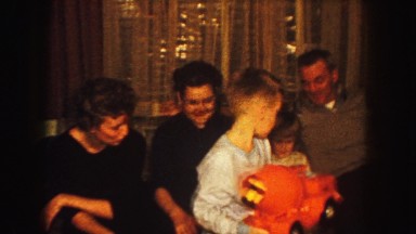 1958: children stand in front of couch presenting a toy as adults look on