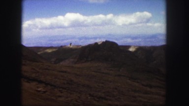 1958: a car and a bus drive along a twisting road winding through hills