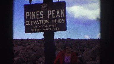1958: lady wearing red coat under pike's peak sign rocks partly cloudy skies