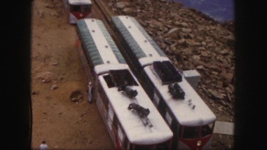 1958: two people by train cars on top of a mountain near the edge of a cliff.