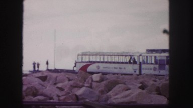 1958: subway train cars are parked on rocky jetty with several people observing