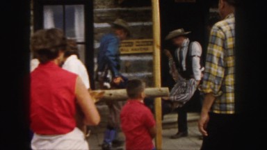 1958: people watching a reenactment, as two actors carry a third inside a log