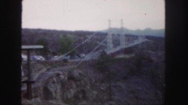 1958: a long suspension bridge crossing a large canyon with cars driving on and