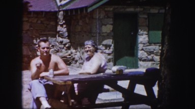 1958: A Man and Woman Sit at a Picnic Table on a Patio in Front of a Stone Building