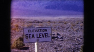 1957: signboard in flat, rock-strewn landscape bounded by hills on horizon