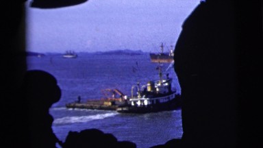 1958: a tug boat gliding through the beautiful blue ocean with a mountain