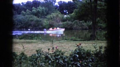 1960: a boat-full of people in the distance travel down the river. WAUCONDA