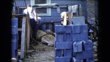 1960: two men roll large rocks away from house foundation during renovation