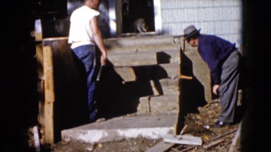 1960: two men at work at entrance of a house where a cat is at the entrance