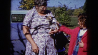 1960: older woman and girl petting dog carried in woman's curved arm