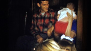 1959: a mother wrestling with her baby in her lap with a man seated next to her