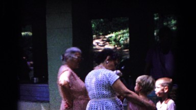 1963: two women smile and laugh at two children outside a house. COLD SPRINGS