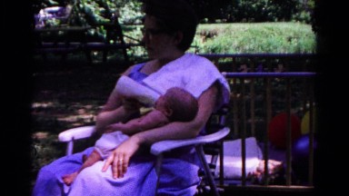 1963: woman in blue dress sits while feeding a baby with a bottle COLD SPRINGS