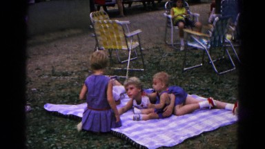 1963: children sit and lay on a blanket and lawn chairs on the ground in a park