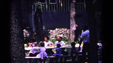 1963: a family gathered outside around a picnic table enjoying lunch together