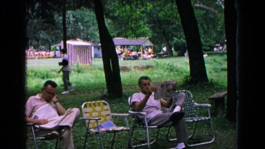 1963: two men in lounge chairs relaxing outdoors as they read the newspaper