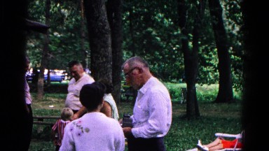 1963: individuals gathered while visiting in an outdoor public shady location