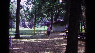 1963: people carry baskets and chairs into picnic area shaded by tall trees