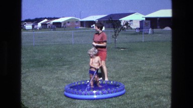 1975: a little boy playing in the pool with a hose while his mother stands by