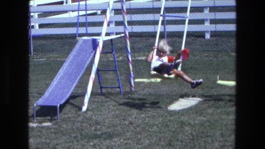 1975: a small child with a red balloon swing on a swing set CALIFORNIA