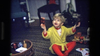 1975: a young boy sits on the floor and lifts up a small gift in each hand.