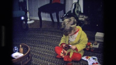 1975: child opening a present and showing it while sitting on the carpet