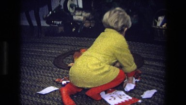 1975: a little boy in pajamas opening a gift on the wrapping paper covered floor
