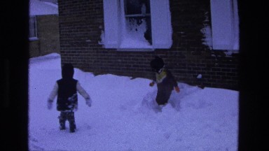 1975: two children bundled in winter clothes trudge through snow