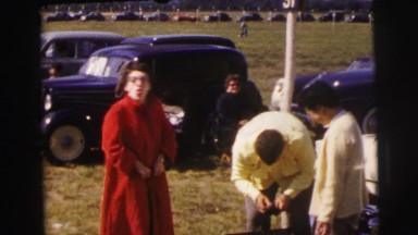 1955: woman in red coat pumps air near vintage cars LE MANS GRAND PRIX, FRANCE