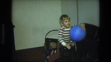 1975: a small boy plays with a blue ball on a string inside his living room