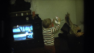 1975: little boy at home showing his father a handmade mask and crown CALIFORNIA