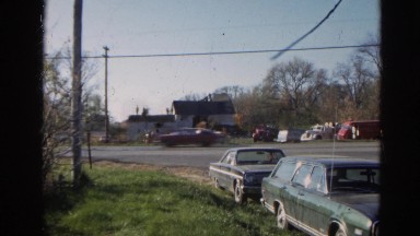 1968: cars parked on the side of the street as traffic passes by