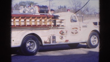 1968: an old fire engine parked by the roadside with a fireman standing