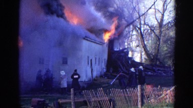 1968: Firefighters Responding to Burning White Building Between Fencing