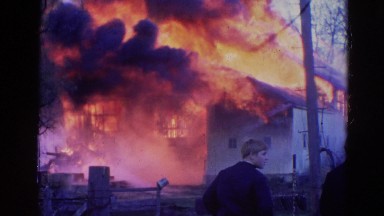 1968: two men outside in the street watching firemen extinguish a blazing fire