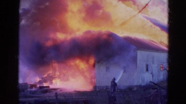 1968: large building engulfed in flames is being attended to by firefighters