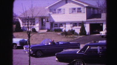 1962: a couple in a convertible pulling out of the driveway and driving down