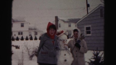 1962: two women enjoy the cold snowy day by building a tall and silly snowman.