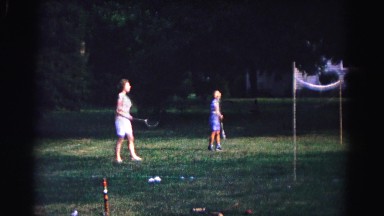1962: woman and boy swinging badminton rackets to hit shuttlecock over net.
