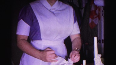 1962: woman in a nurse outfit carefully unwraps and then opens a box