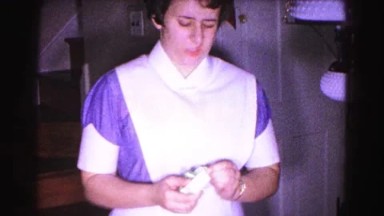1962: solemn nurse in old timey outfit unboxing gold necklace jewelry