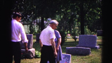 1962: men and woman in a dress standing in a cemetery overlooking a grace stone