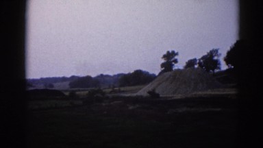 1962: barren land with abandoned house, heap of sand, and sparse vegetation