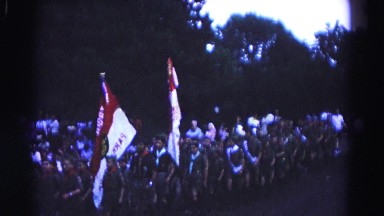 1966: shows a parade of boy scout troop marching down street with flags.