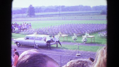 1966: two men are pulling something out of a hearse on a high school track