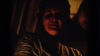 1964: a lady and a little girl sit smiling and talking in a dim living room.
