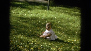 1964: a chubby cheeked baby girl in a white dress sits in the grass HAWAII