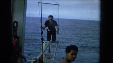 1964: Man in Black Shirt and Pants Balancing on Beam Aboard Boat in Hawaii