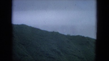 1964: the coastline of a quiet body of water approaching the foot of a green
