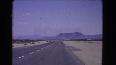 1966: vehicle is slowly moving over a paved road through a desert expanse.